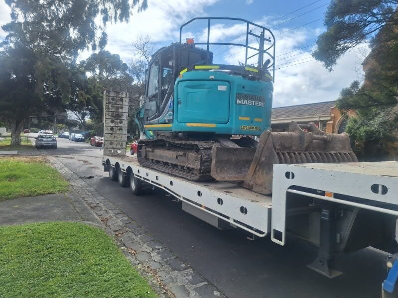 Teal Demolition Masters Kobelco excavator loaded on a float trailer on a suburban Melbourne street