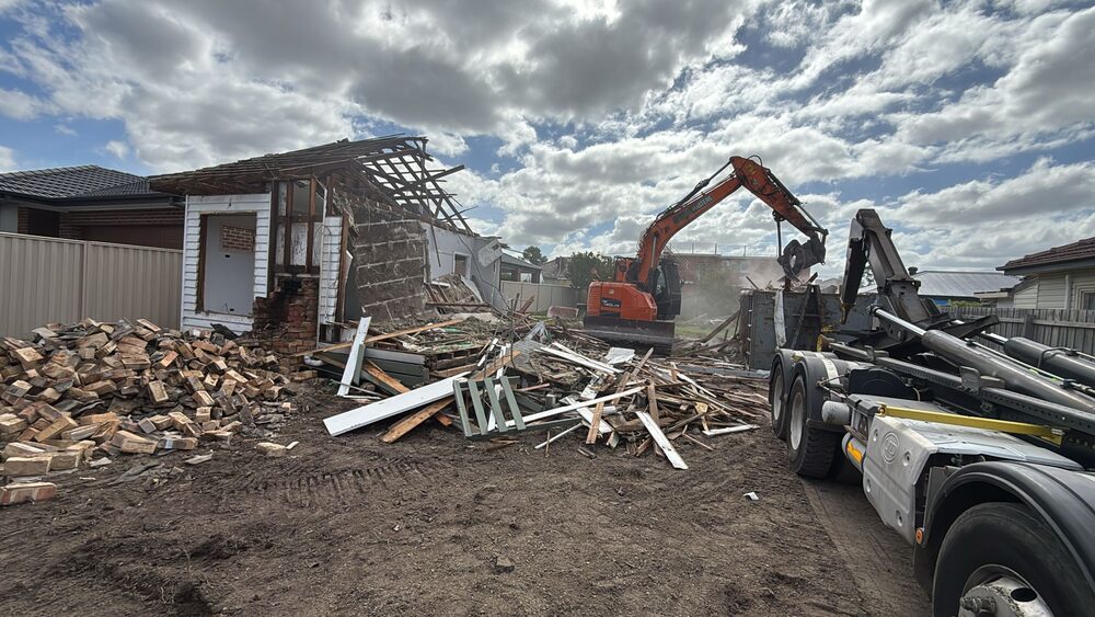 Demolition Masters hook lift truck collecting a full bin from a residential demolition site